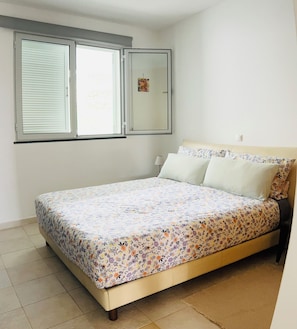 Une chambre Ă coucher avec un lit, une fenĂȘtre avec des stores, une table de chevet et un miroir.