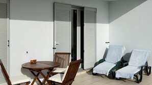 Un balcon avec une table ronde en bois et des chaises, deux fauteuils de jardin et une porte coulissante.