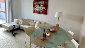 Un salon moderne avec une table à manger en verre, des chaises blanches, un canapé et un tableau abstrait rouge accroché au mur.