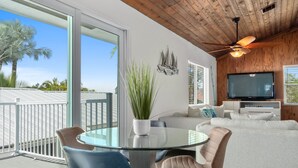 A modern living room with a glass dining table, comfortable seating, a television, and a view of the outdoors. - 5BR/4.5B Beach House- heated pool, deep water dock, walk to beach! (Fort Pierce)
