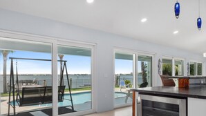 A modern kitchen with a large island, sliding glass doors leading to a pool area, and a view of the water. - 5BR/4.5B Beach House- heated pool, deep water dock, walk to beach! (Fort Pierce)