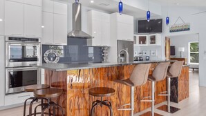 A modern kitchen with white cabinets, stainless steel appliances, and a wooden island with bar stools. - 5BR/4.5B Beach House- heated pool, deep water dock, walk to beach! (Fort Pierce)