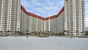 Un hotel de gran altura con varios balcones, vista a la playa y un primer plano con arena.