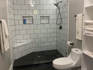 A bathroom with white tiled walls, a black shower floor, a white toilet, and a towel rack. - East Wind - 4 Bedroom Ocean Front Luxury (Utila)