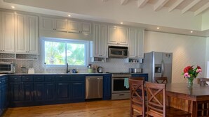 A modern kitchen with dark blue cabinets, stainless steel appliances, and a wooden dining table with chairs.