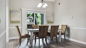 Un comedor con una mesa y seis sillas, una ventana con vista a follaje y un candelabro en el techo.