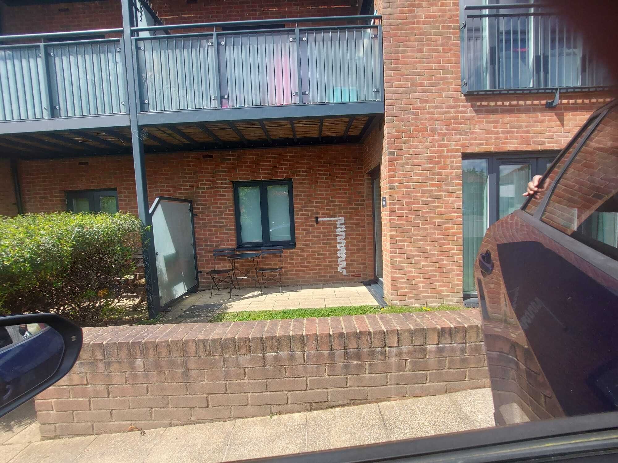 A two-story brick building with a balcony, a small outdoor seating area, and a car parked in front.