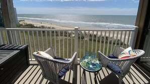 Un balcon avec des fauteuils en osier et une table en verre donnant sur une plage.