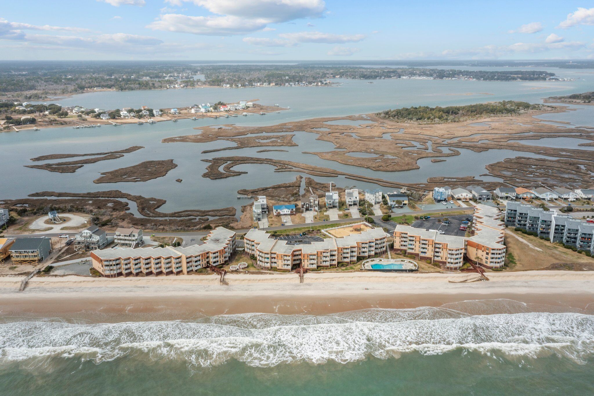 An aerial view of a coastal hotel with multiple buildings, a beach, and a large body of water.