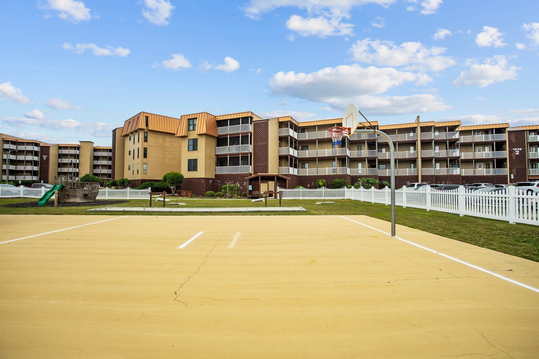 A multi-story residential building with a basketball court in front.