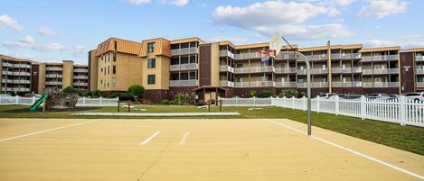 A multi-story residential building with a basketball court in front.
