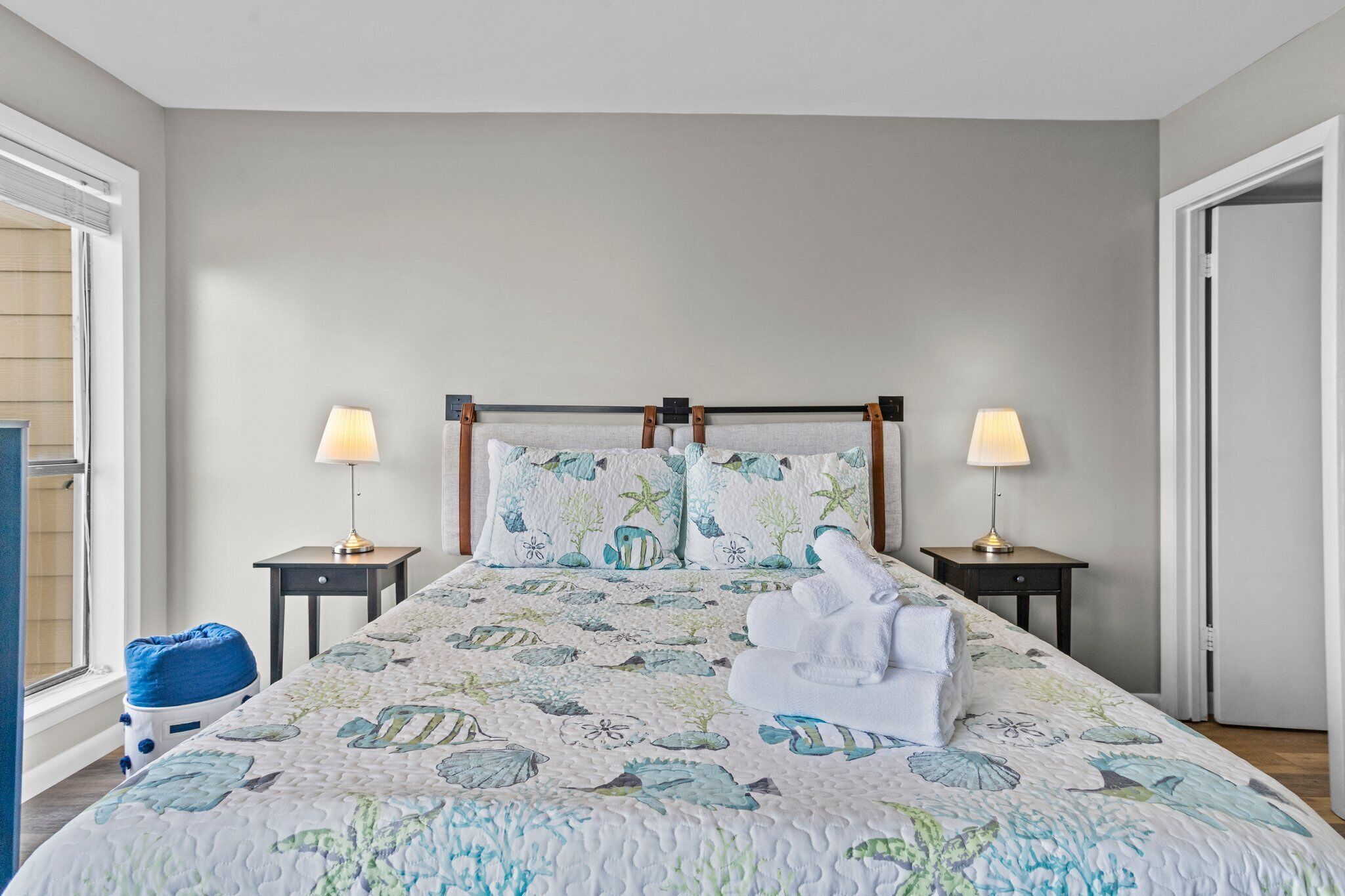 A neatly made bed with a floral bedspread, two bedside lamps, and a blue bean bag chair.