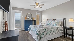 Une chambre à coucher comprenant un lit, un ventilateur de plafond, un bureau, une chaise, une commode, un miroir et une vue sur l’océan.