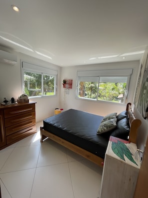 Un dormitorio con cama, cómoda de madera y dos ventanas.