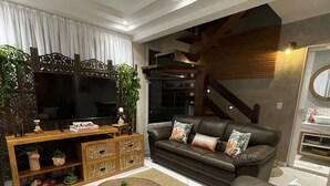 A modern living room with a brown leather sofa, a wooden coffee table, and a TV on a wooden stand. - High standard, beachfront. (Ubatuba)