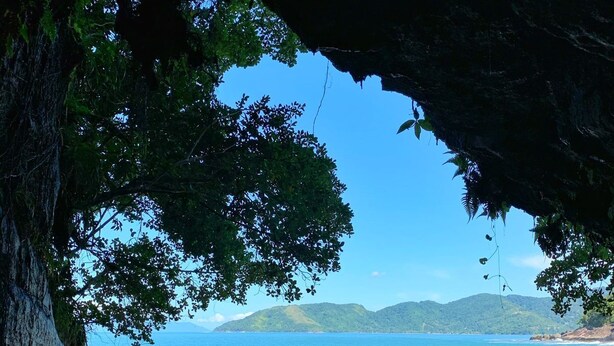 A beach scene with a cave entrance, clear blue water, and distant hills. - High standard, beachfront. (Ubatuba)