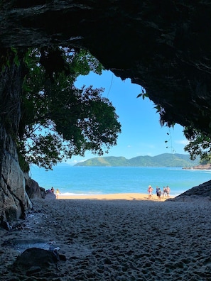 A beach scene with a cave entrance, clear blue water, and distant hills. - Luxury, right on the beach. (Ubatuba)