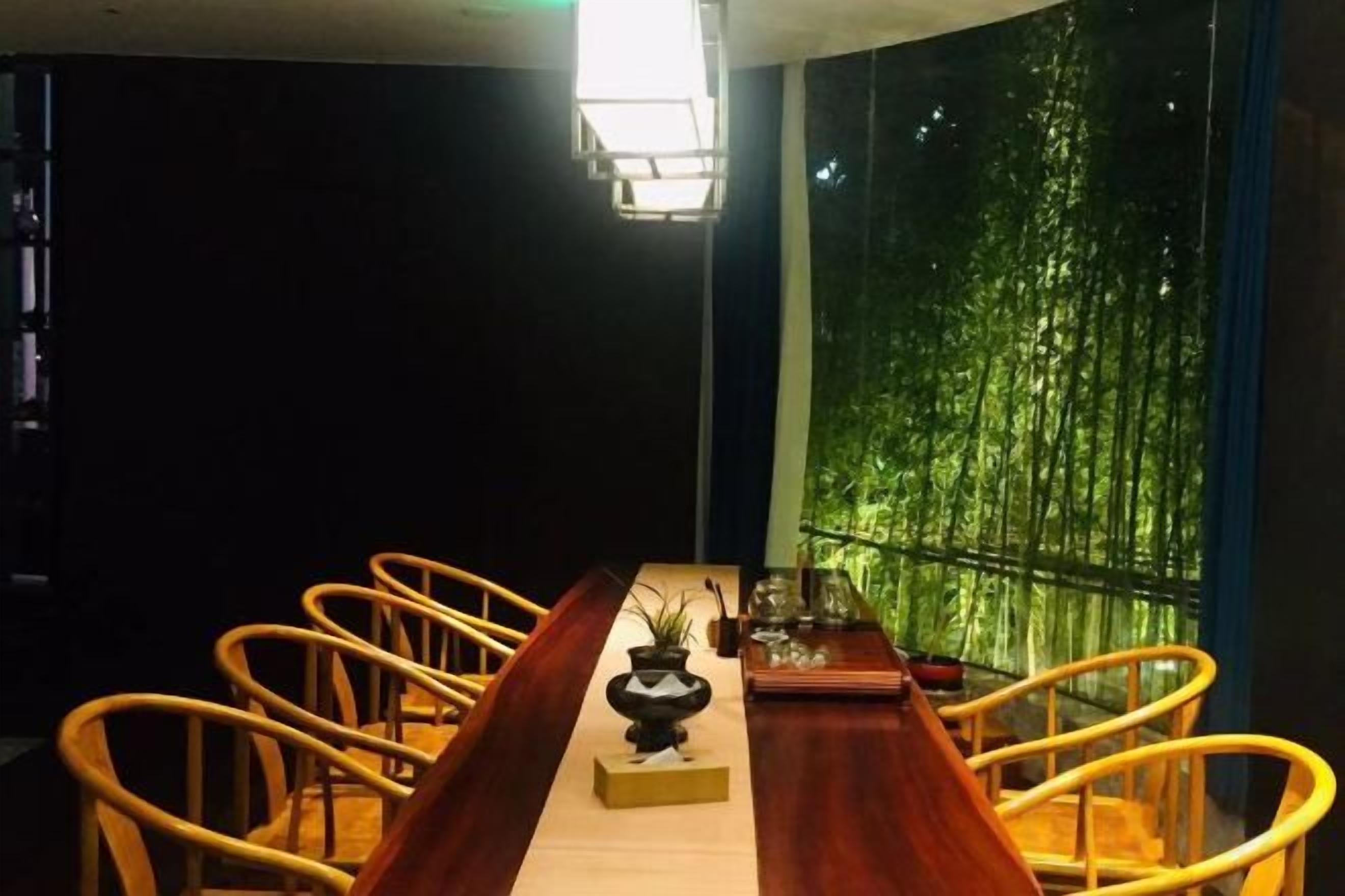Un comedor con una mesa larga, sillas y vistas al bambú.