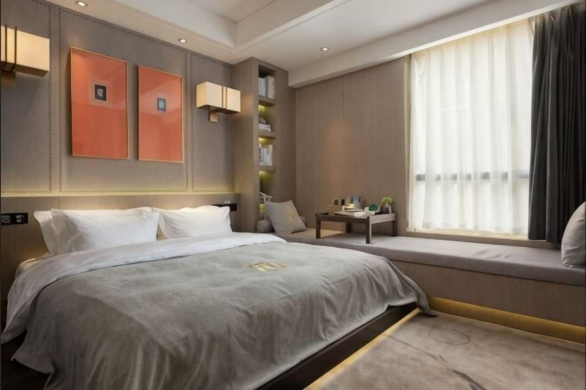 Una habitación de hotel con cama, mesita de noche, asiento junto a la ventana y estantes en la pared.