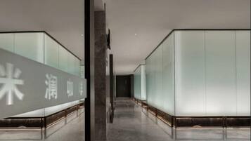 A corridor with mirrored walls and a reflective floor, leading to a room with a large mirror and a door.