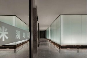 A corridor with mirrored walls and a reflective floor, leading to a room with a large mirror and a door.
