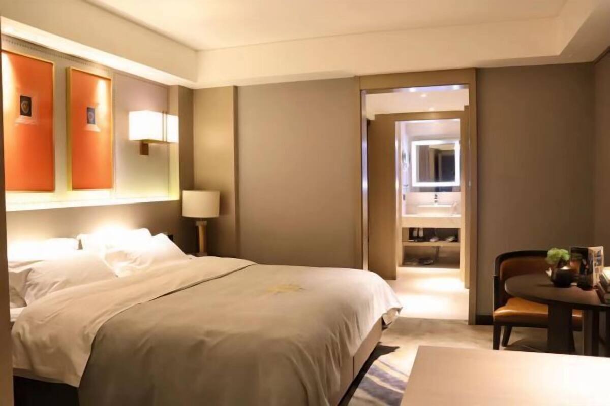 Una habitación de hotel con cama, escritorio, silla, lámpara y espejo.