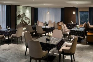 A hotel dining area with multiple tables and chairs, a large painting on the wall, and a view of the outdoors through the windows. - yueTing Chain Hotel (Hanyuan)