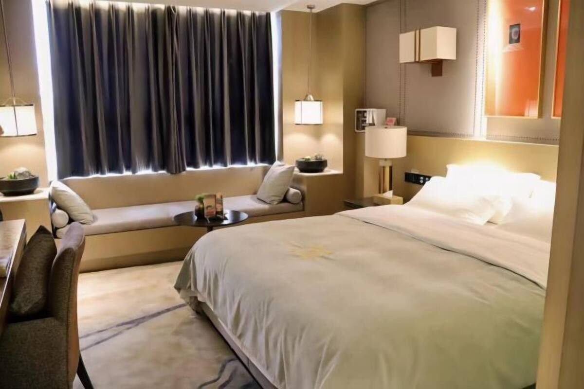 Habitación de hotel con una cama grande, un sofá cama, una mesita con lámpara y una ventana con cortinas.