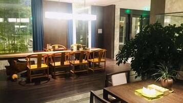 Un espace repas avec une longue table et des chaises, une plante en pot et une vue dégagée grâce à de grandes fenêtres.