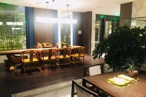 A dining area with a long table and chairs, a potted plant, and a view through large windows. - yueTing Chain Hotel (Hanyuan)