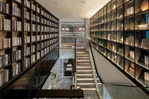 A library with bookshelves on both sides, a central staircase, and a marble floor. - yueTing Chain Hotel (Hanyuan)