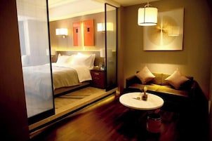 A hotel room with a bed, a sofa, a small table, and a wall-mounted lamp.