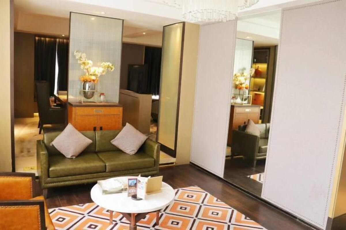 Una habitación de hotel moderna con un sofá verde, una mesa de centro redonda y un espejo grande.