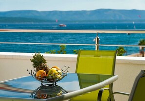 A table with a fruit bowl on a balcony overlooking a body of water with boats.