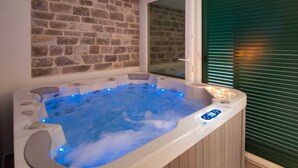 A hot tub with blue LED lights, a stone wall, and a window with blinds. - Luxury Villa Old Story with Pool (Bol)