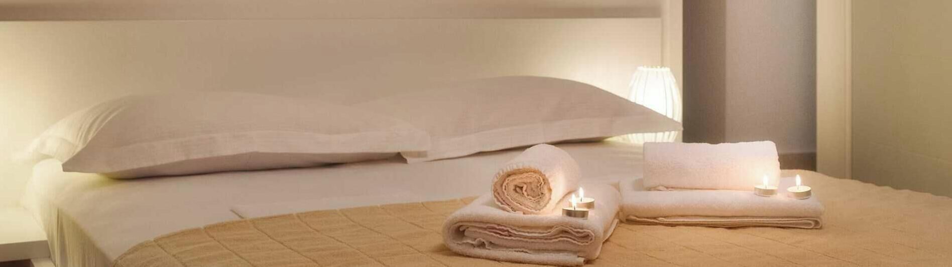 A hotel room with a bed, a wall with motivational text, and a small table with towels and candles.