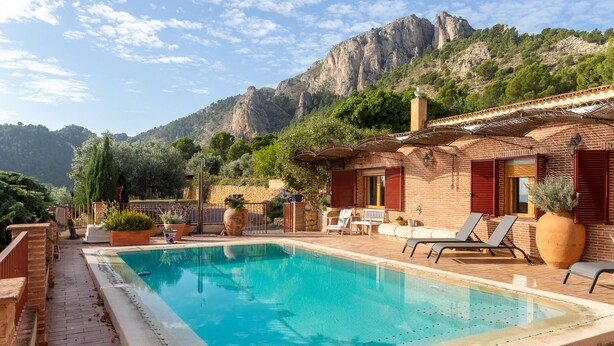 A pool area with a clear blue pool, lounge chairs, and a mountain backdrop.