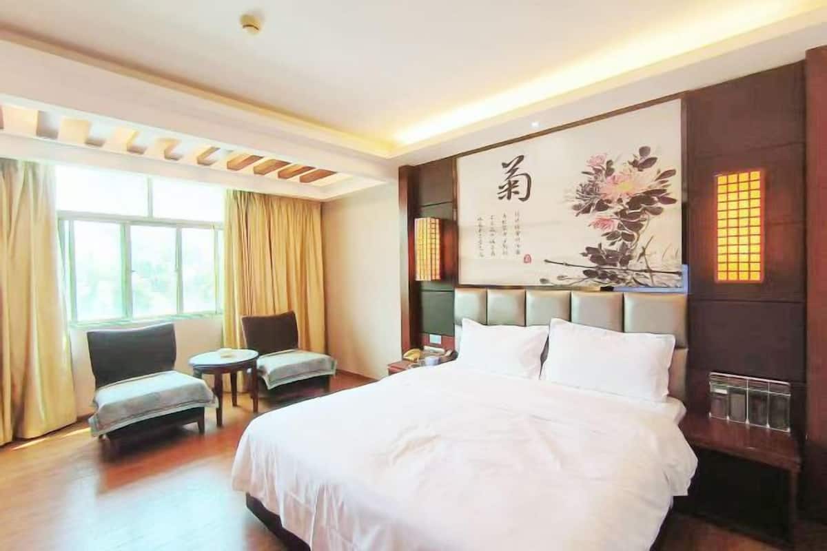 Habitación de hotel con una cama grande, una zona de estar con dos sillones, una mesita y un adorno en la pared.