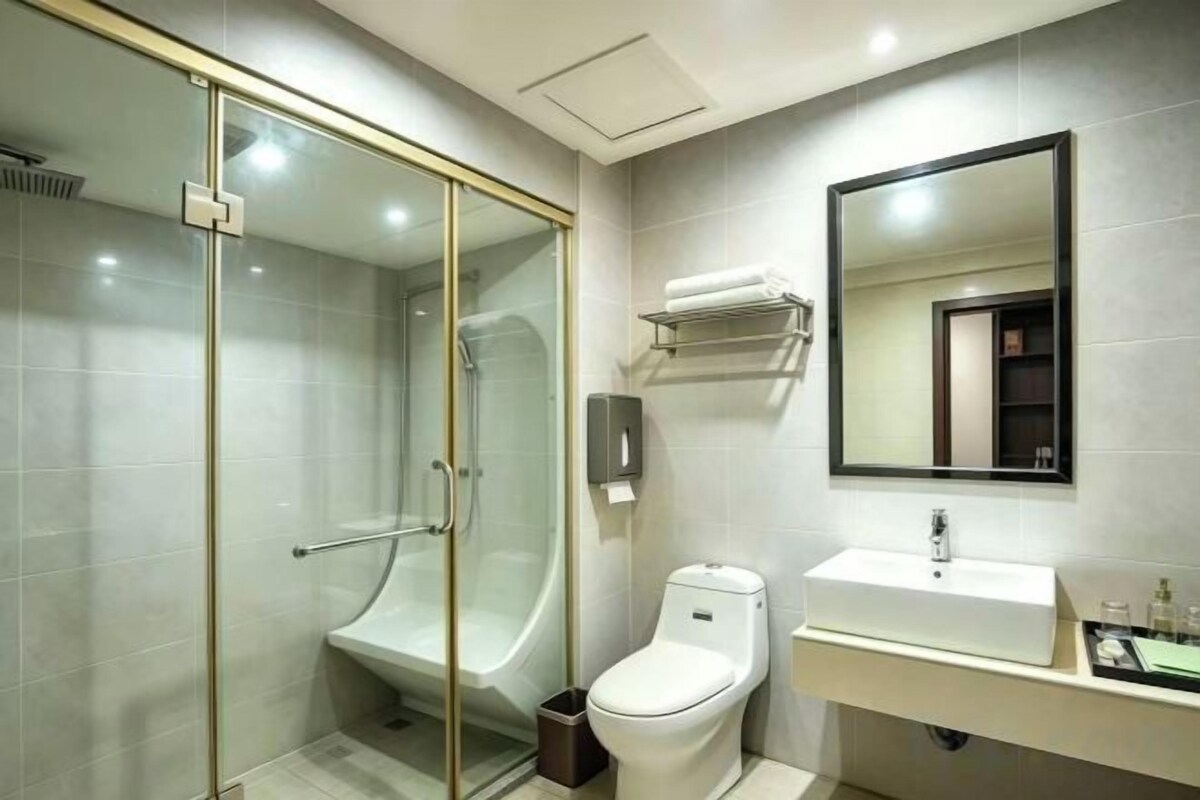 A modern bathroom with a glass-enclosed shower, a white toilet, and a sink with a mirror above it.