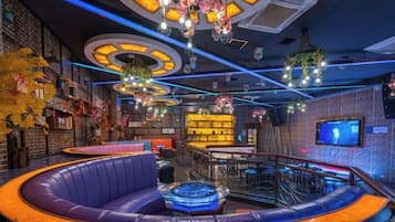 A bar area with a curved seating arrangement, a pool table, and a television screen on the wall.