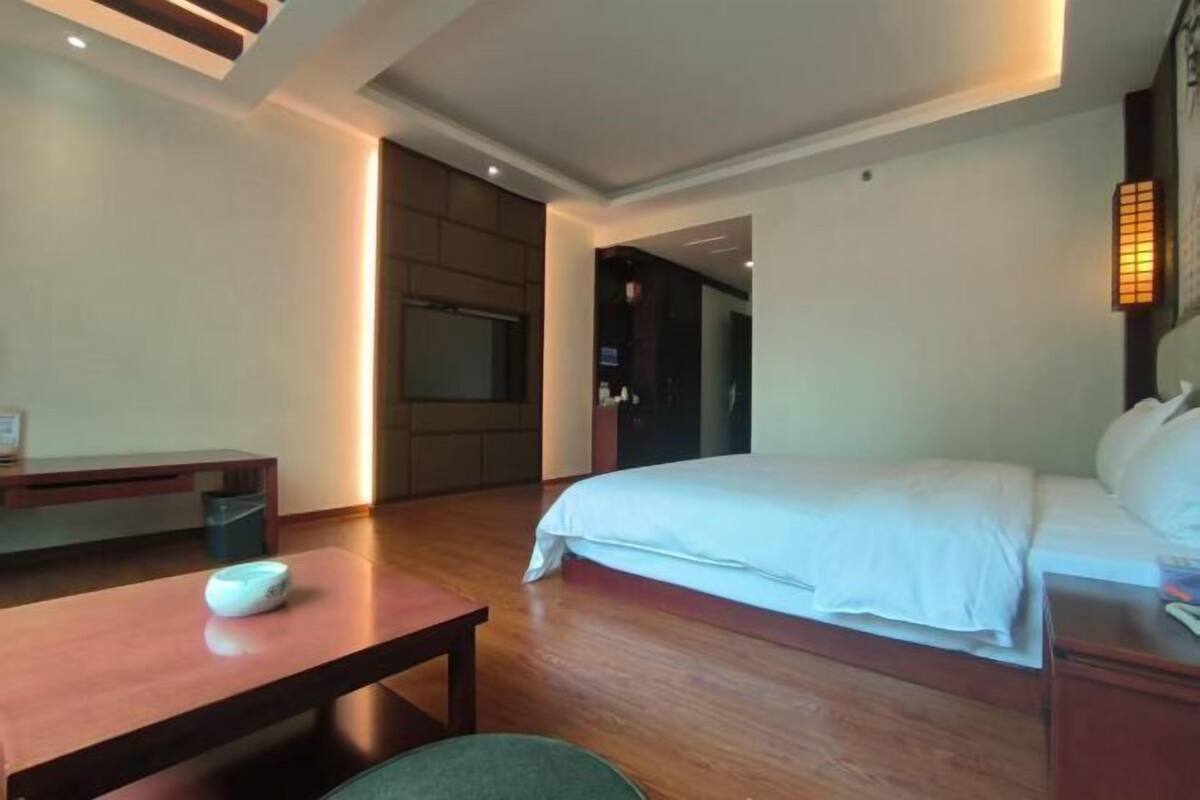 Habitación de hotel con cama, escritorio y silla. Hay un televisor en la pared y una puerta que da a otra habitación.