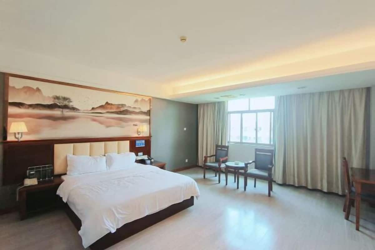 Habitación de hotel con una cama grande, un escritorio, dos sillas, un cuadro en la pared y una ventana con cortinas.