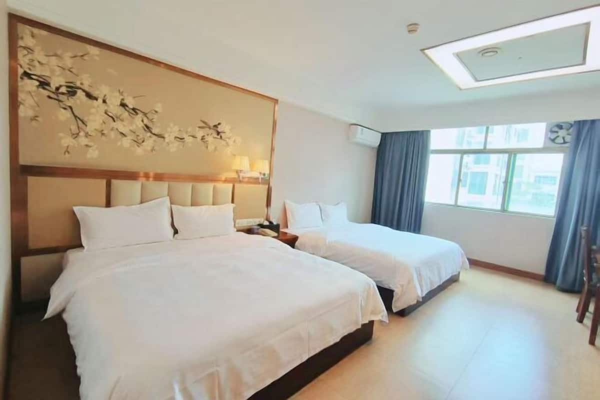 Habitación de hotel con dos camas, un adorno en la pared, una ventana con cortinas e iluminación en el techo.