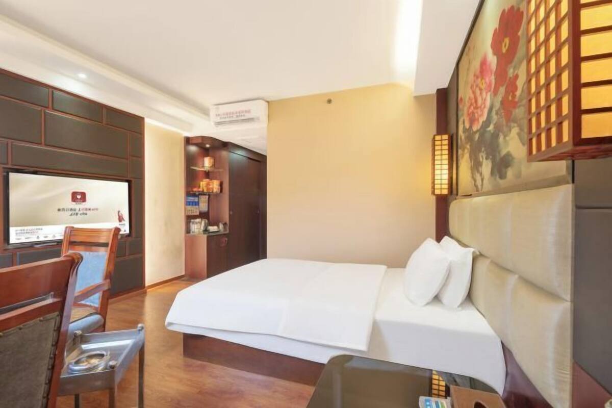 Habitación de hotel con cama, televisor montado en la pared, una silla de madera y una mesita.