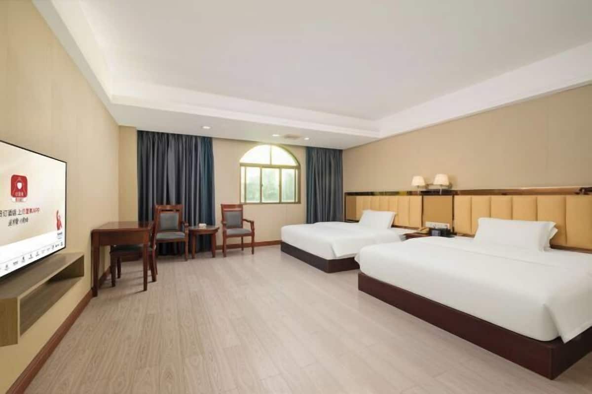 Habitación de hotel con dos camas, televisión, escritorio y ventana con cortinas.