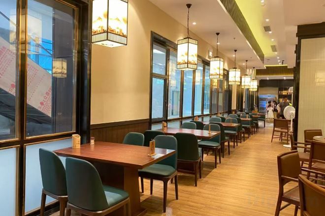 A restaurant with long tables and chairs, large windows, and hanging lights.