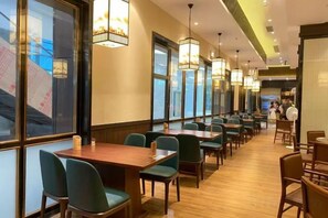 A restaurant with long tables and chairs, large windows, and hanging lights. - Shuncheng Hotel (Dongguan)