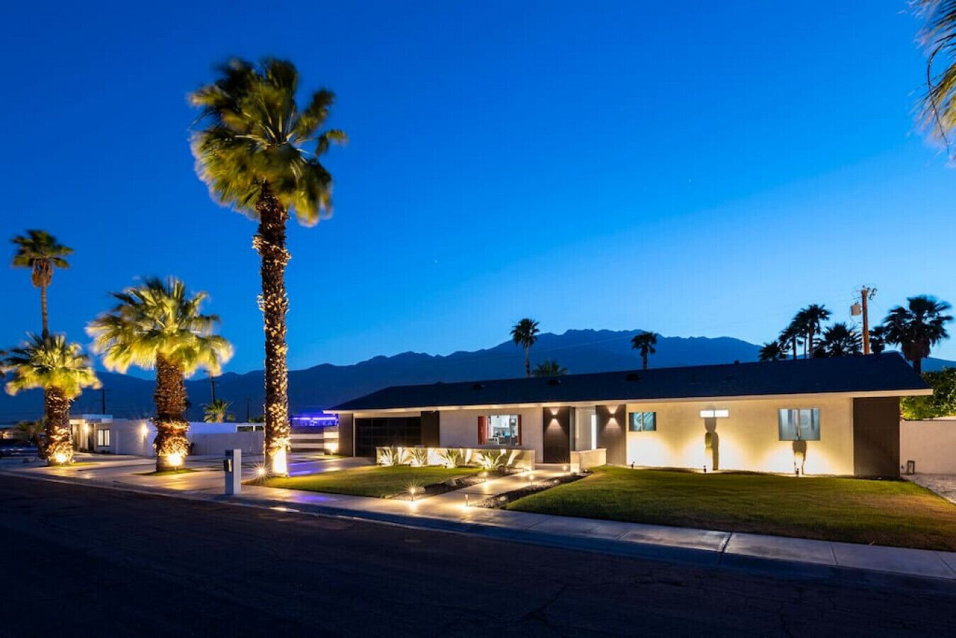 A modern building with a flat roof, surrounded by palm trees and a mountain backdrop.