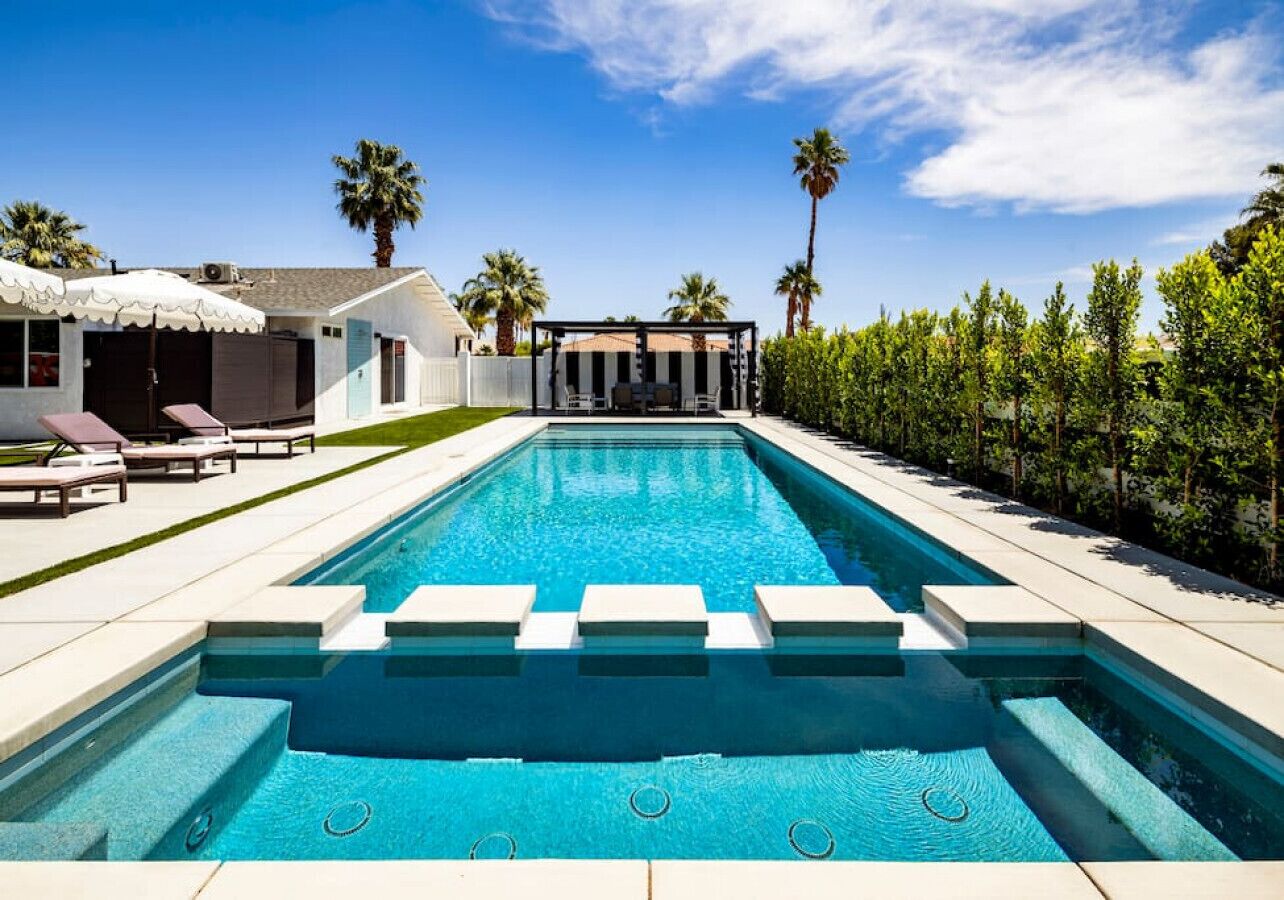 Une piscine rectangulaire à l’eau d’un bleu cristallin, entourée d’une terrasse blanche et de chaises longues.