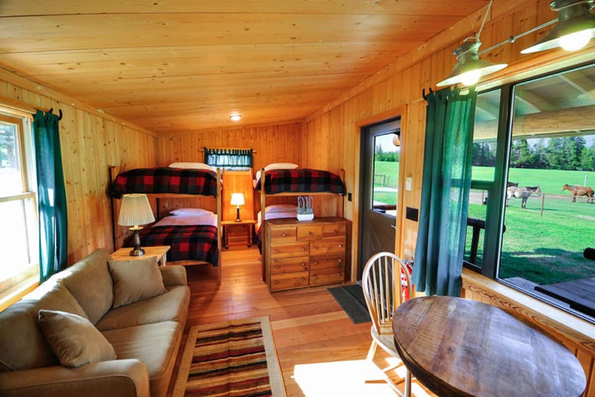A cabin with two bunk beds, a sofa, a wooden dresser, and a dining table.